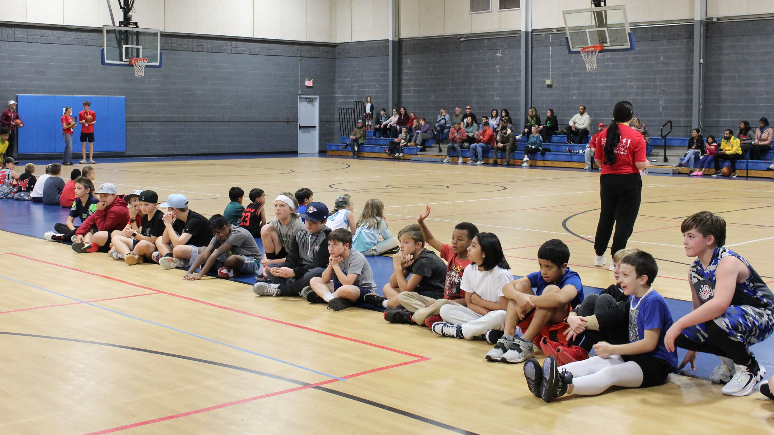 kids sitting in a line on a basketball court floor